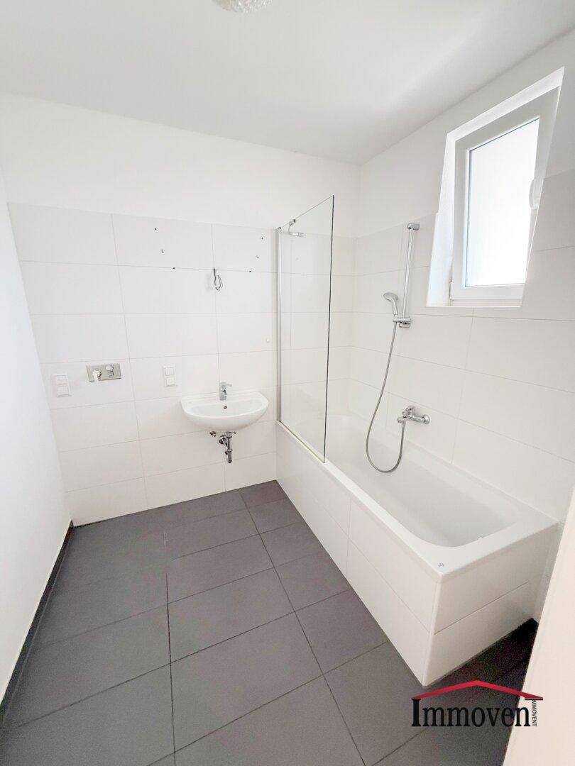 Helles Badezimmer mit Badewanne, Duschabtrennung, Waschbecken und einem Fenster für natürliche Belüftung.