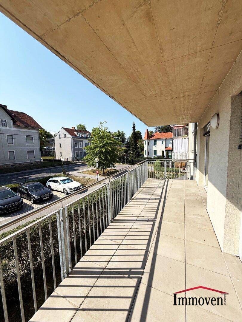 Heller Balkon mit Fliesenboden und freiem Blick auf die Straße und umliegende Gebäude.