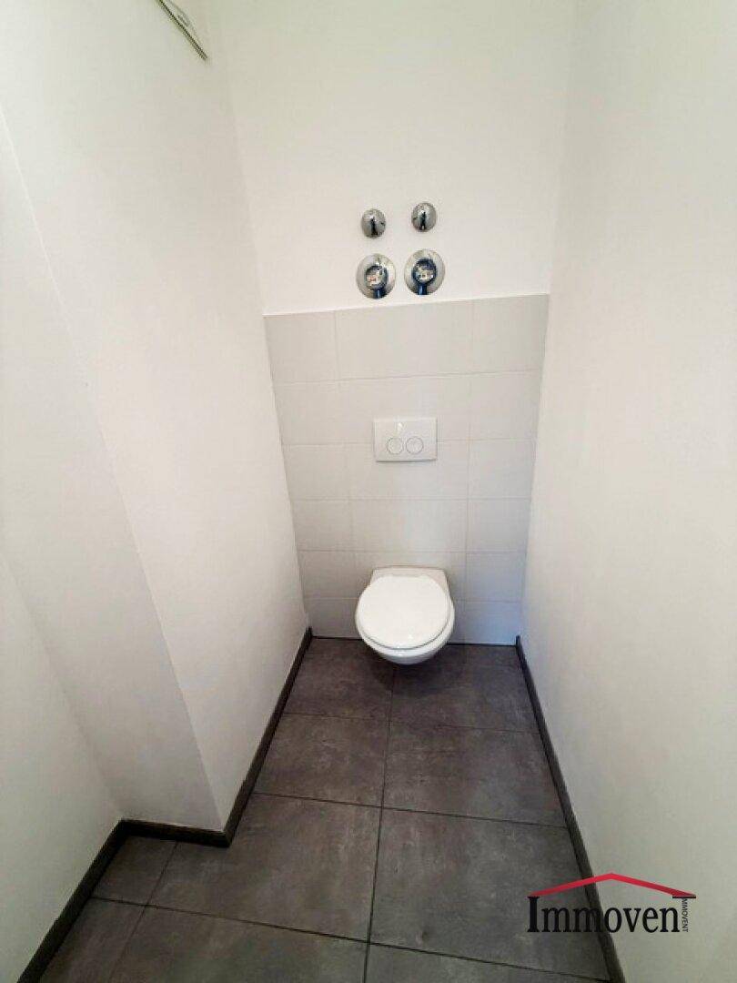 Separates WC mit wandhängender Toilette und modernen grauen Bodenfliesen, sauber und funktional.