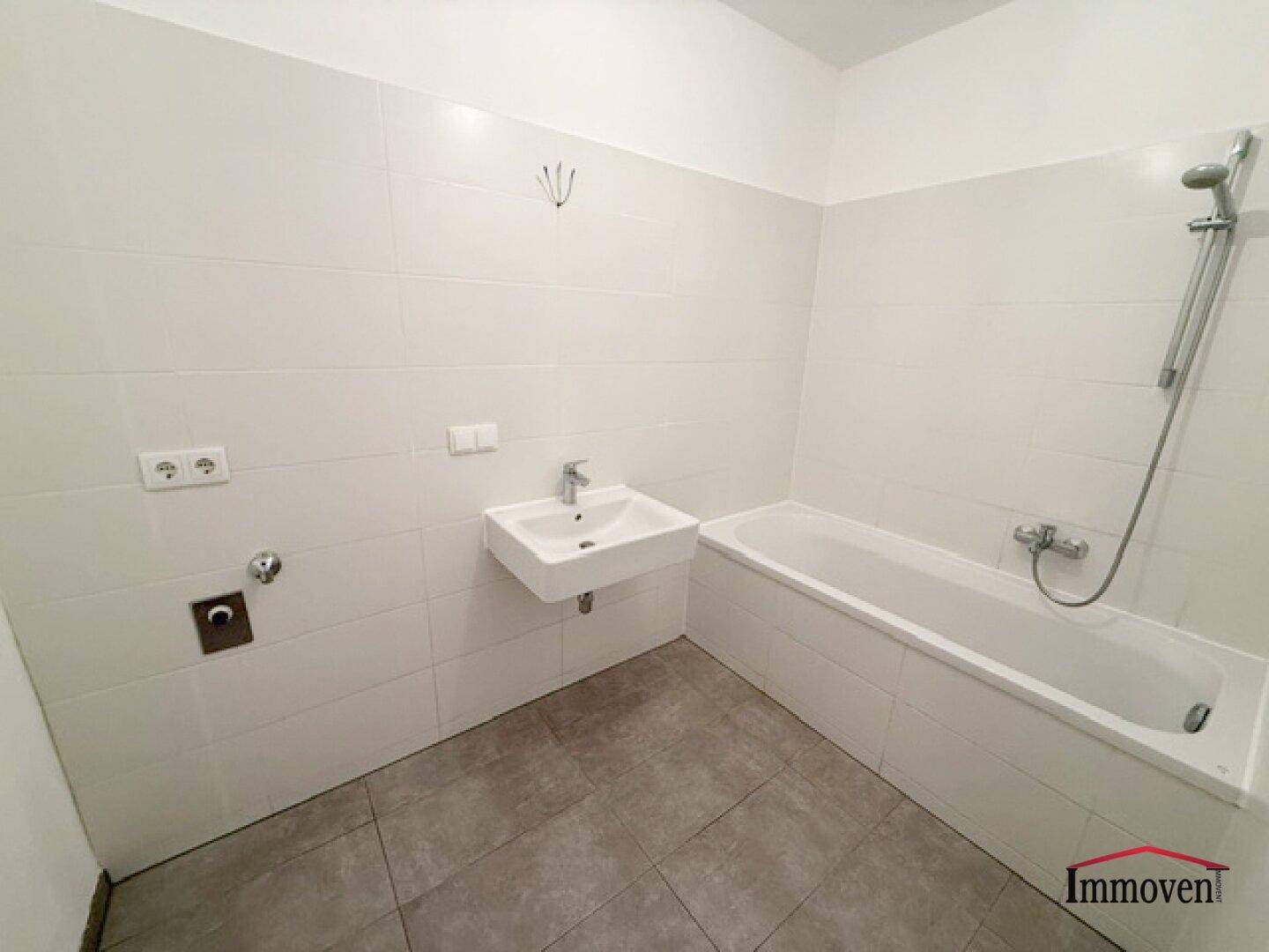 Modernes Badezimmer mit weißen Fliesen, Badewanne und Waschbecken, in gutem Zustand.