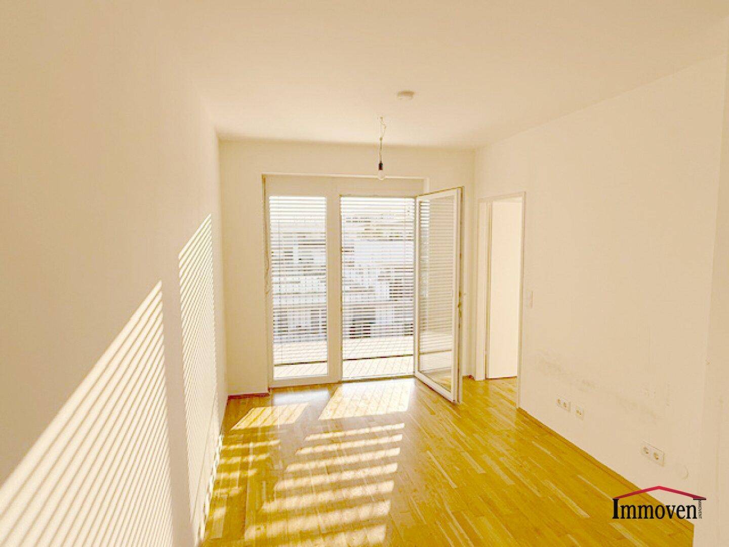 Helles Wohnzimmer mit Parkettboden und Zugang zu einem Balkon, durchflutet von Sonnenlicht.