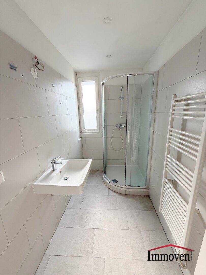 Helles Badezimmer mit Duschkabine, Waschbecken, Fenster und beheiztem Handtuchhalter.