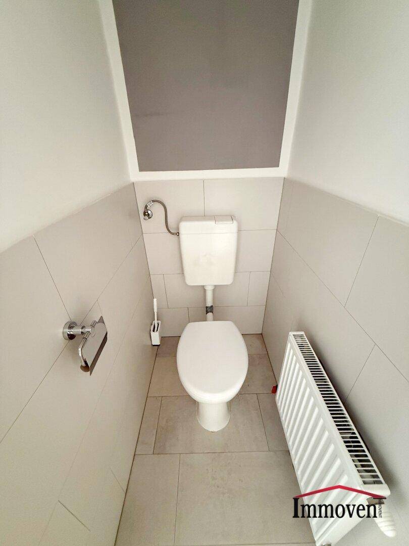 Separates WC mit Toilette, Heizkörper und hellen Fliesen an Wänden und Boden.