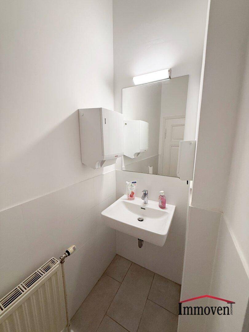 Kleiner Toilettenraum mit Waschbecken, Spiegel und Heizkörper, sauber und funktional.
