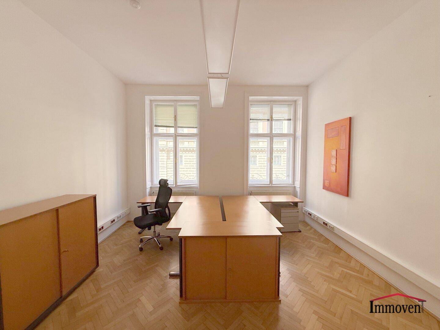 Einzelbüro mit klassischem Fischgrätparkett, großen Fenstern und moderner Kunst an der Wand.