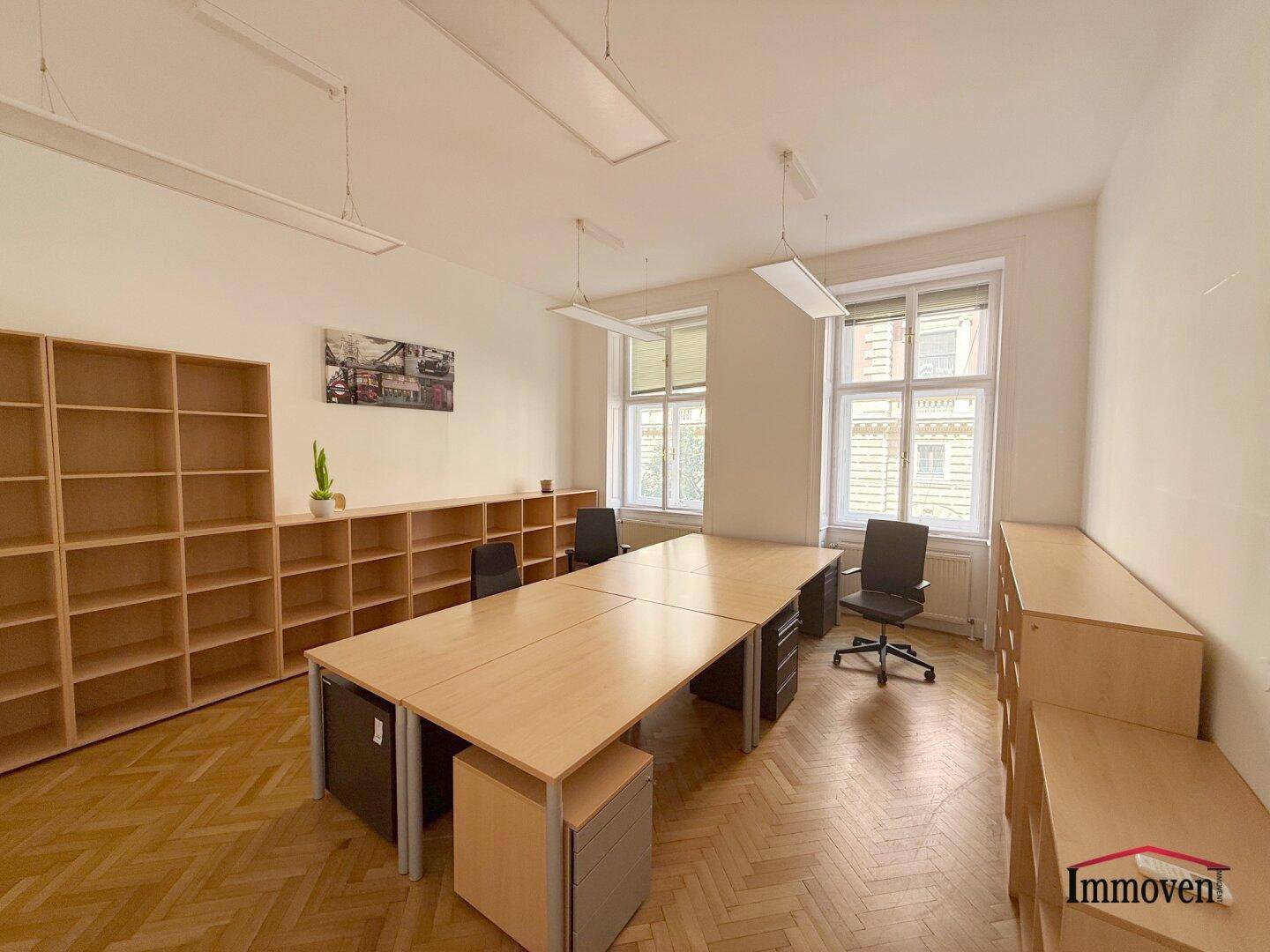Helles Büro mit Holzparkett, Regalen und mehreren Schreibtischen, ideal für ein Team.