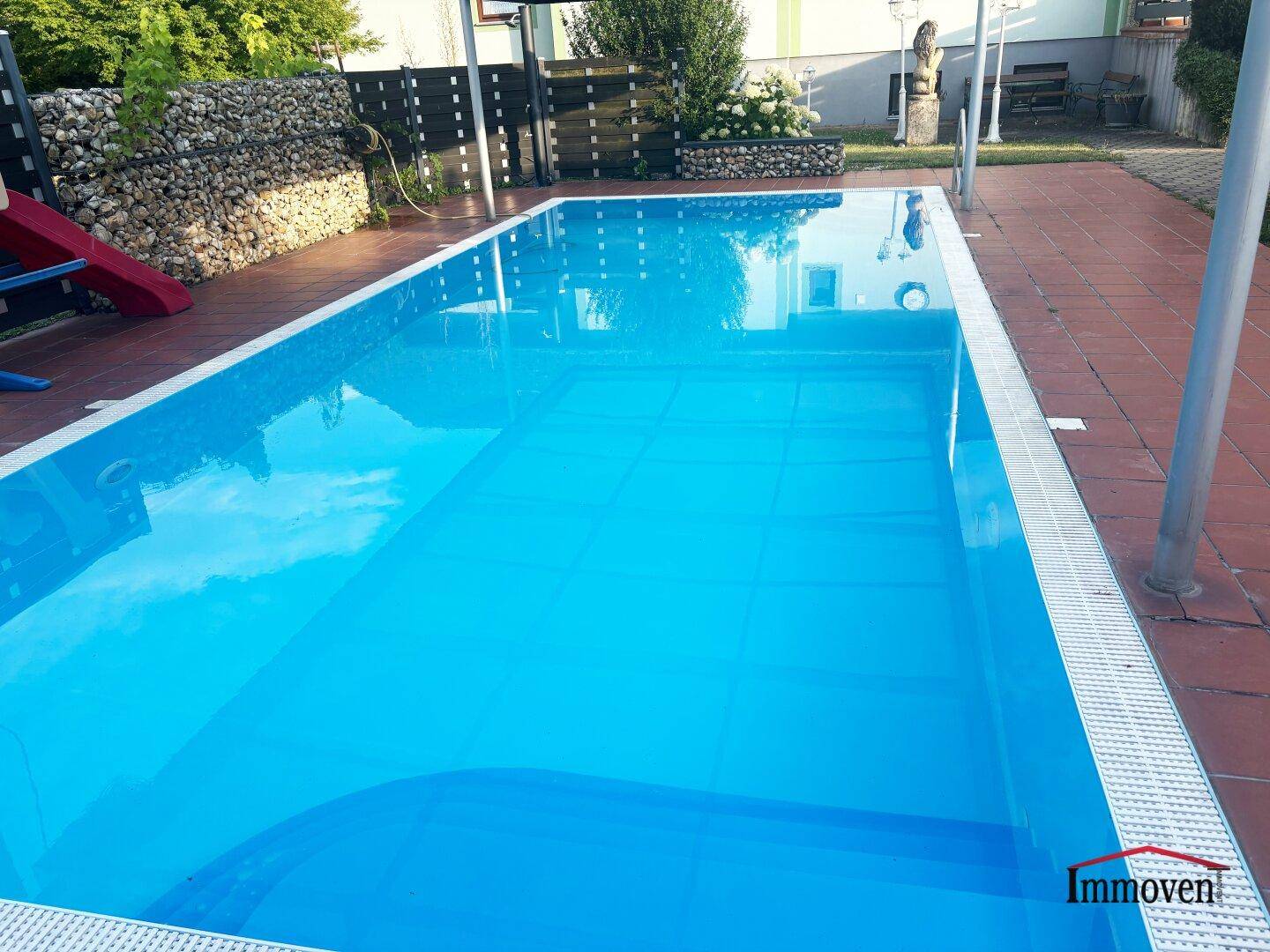 Großer Swimmingpool mit blauer Auskleidung und Treppeneinstieg, umgeben von einer Terrasse.