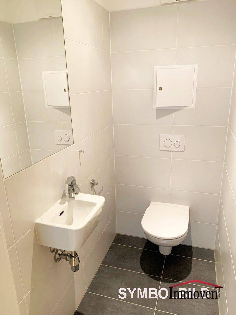 Gäste-WC mit wandhängendem WC, kleinem Waschbecken und modernen Fliesen.