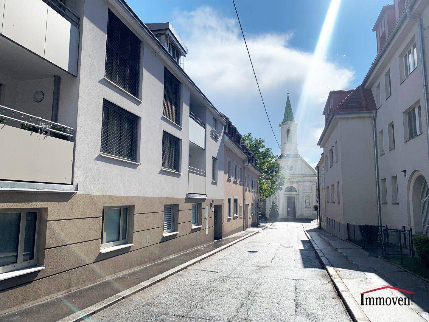 Ruhige Wohnstraße mit Gebäuden und einer Kirche im Hintergrund.