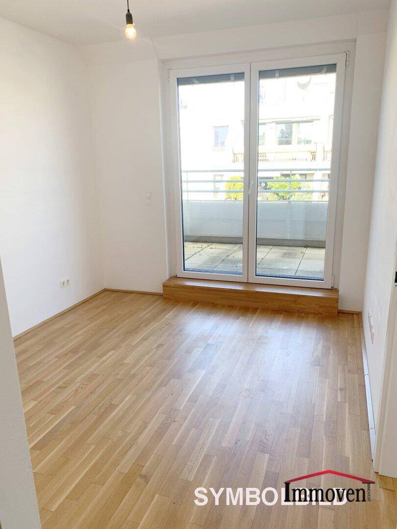 Helles Zimmer mit Parkettboden und großem Fenster mit Zugang zum Balkon.