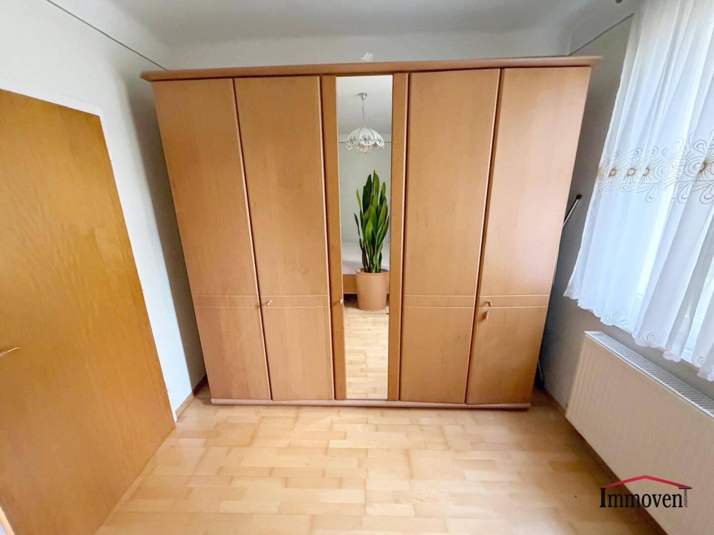 Schlafzimmer mit großem Holzschrank und Spiegeltür, bietet viel Stauraum und einen hellen Parkettboden.