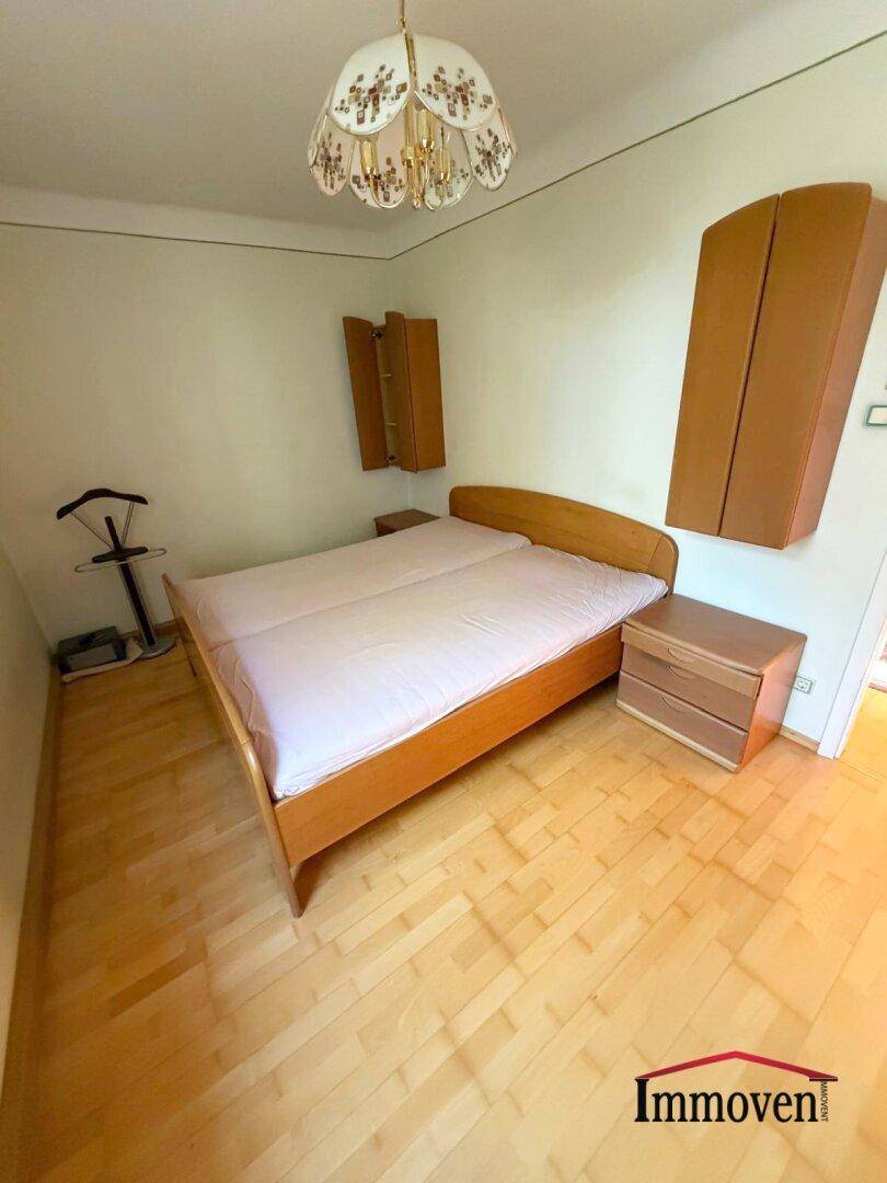 Schlafzimmer mit Doppelbett, Nachttischen und Holzparkett, beleuchtet von einer klassischen Deckenleuchte.