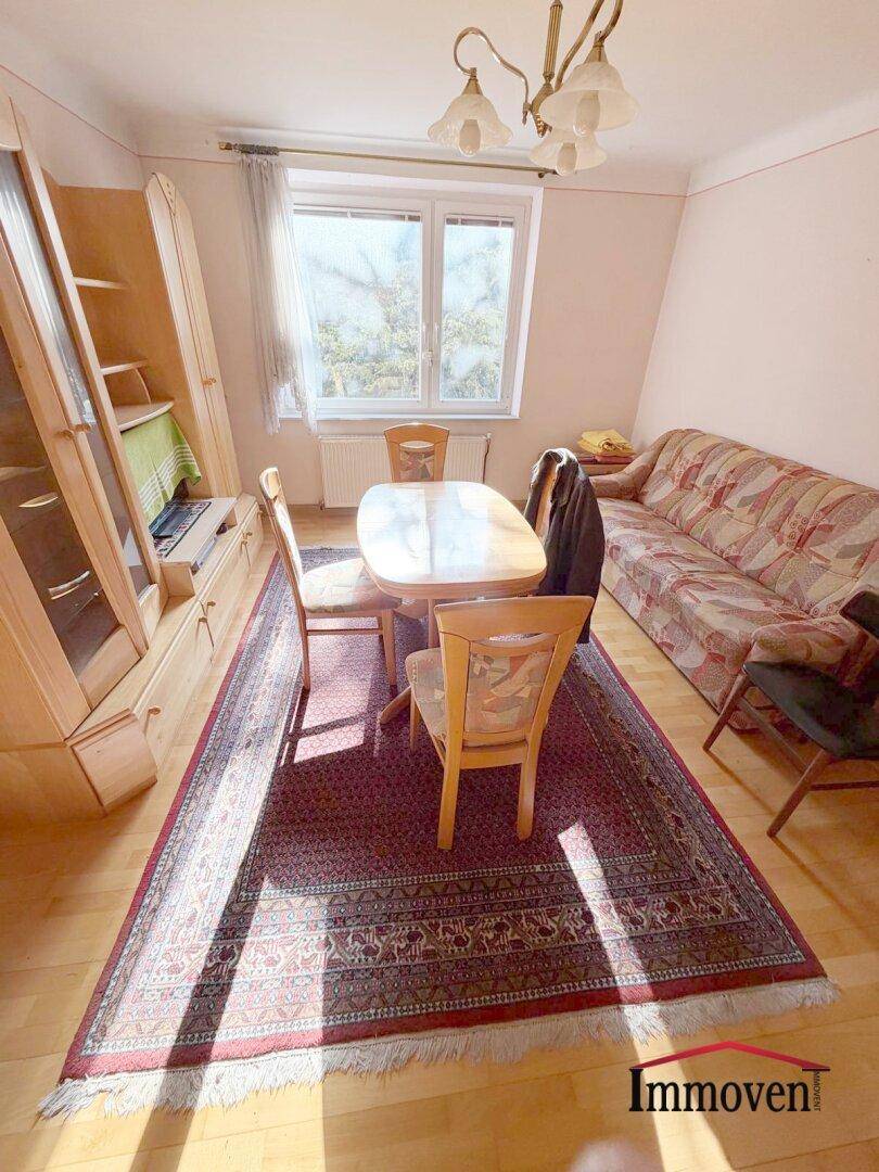 Helles Wohnzimmer mit Esstisch, Sofa und Holzmöbeln, durchflutet von natürlichem Licht durch das Fenster.