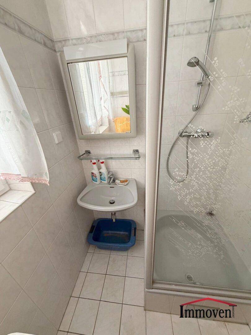 Kleines Badezimmer mit Dusche, Waschbecken und hellen Fliesen, ausgestattet mit einem Spiegelschrank.