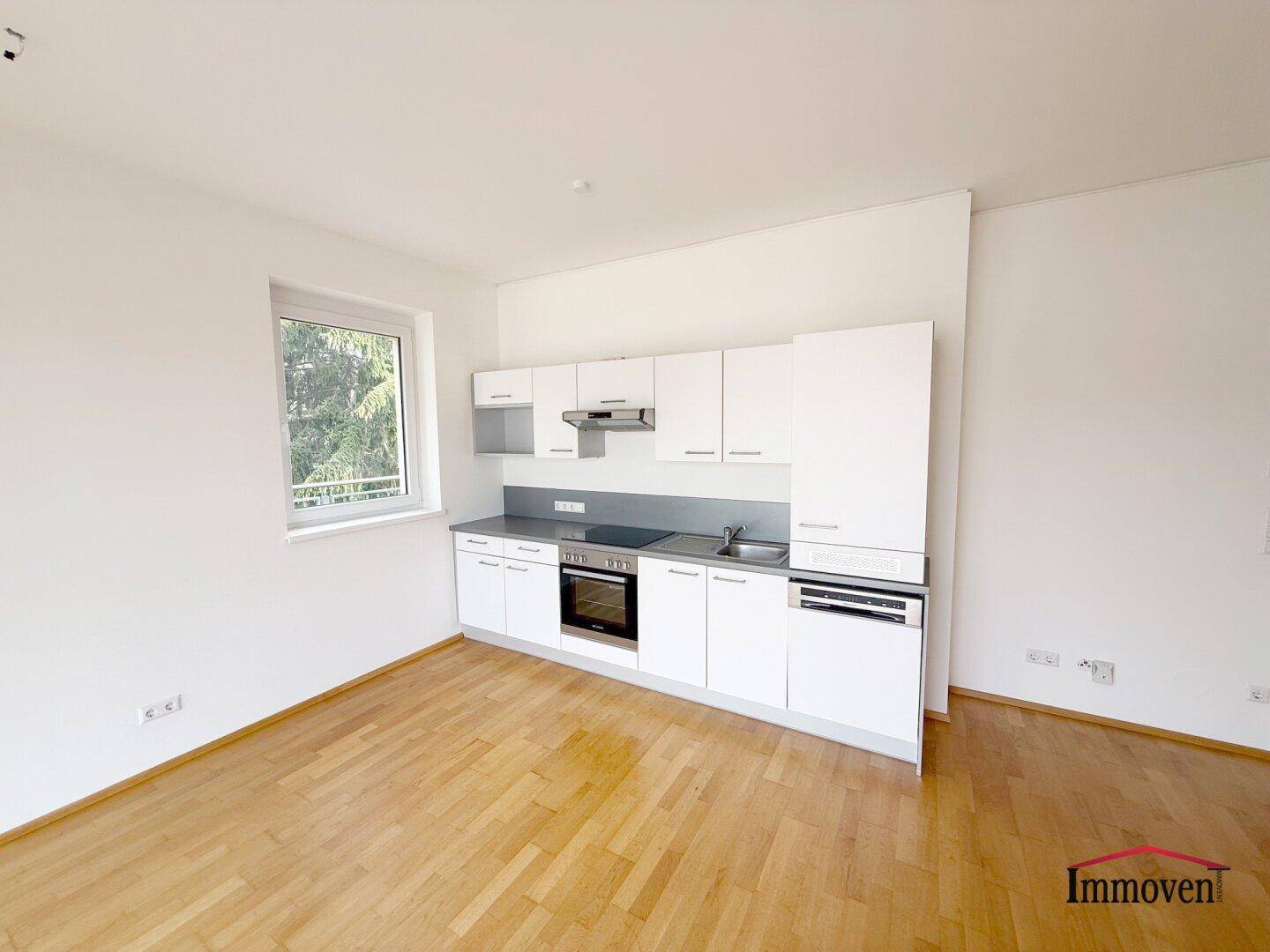 Moderne weiße Einbauküche mit integrierten Geräten in einem hellen Raum mit Holzboden.