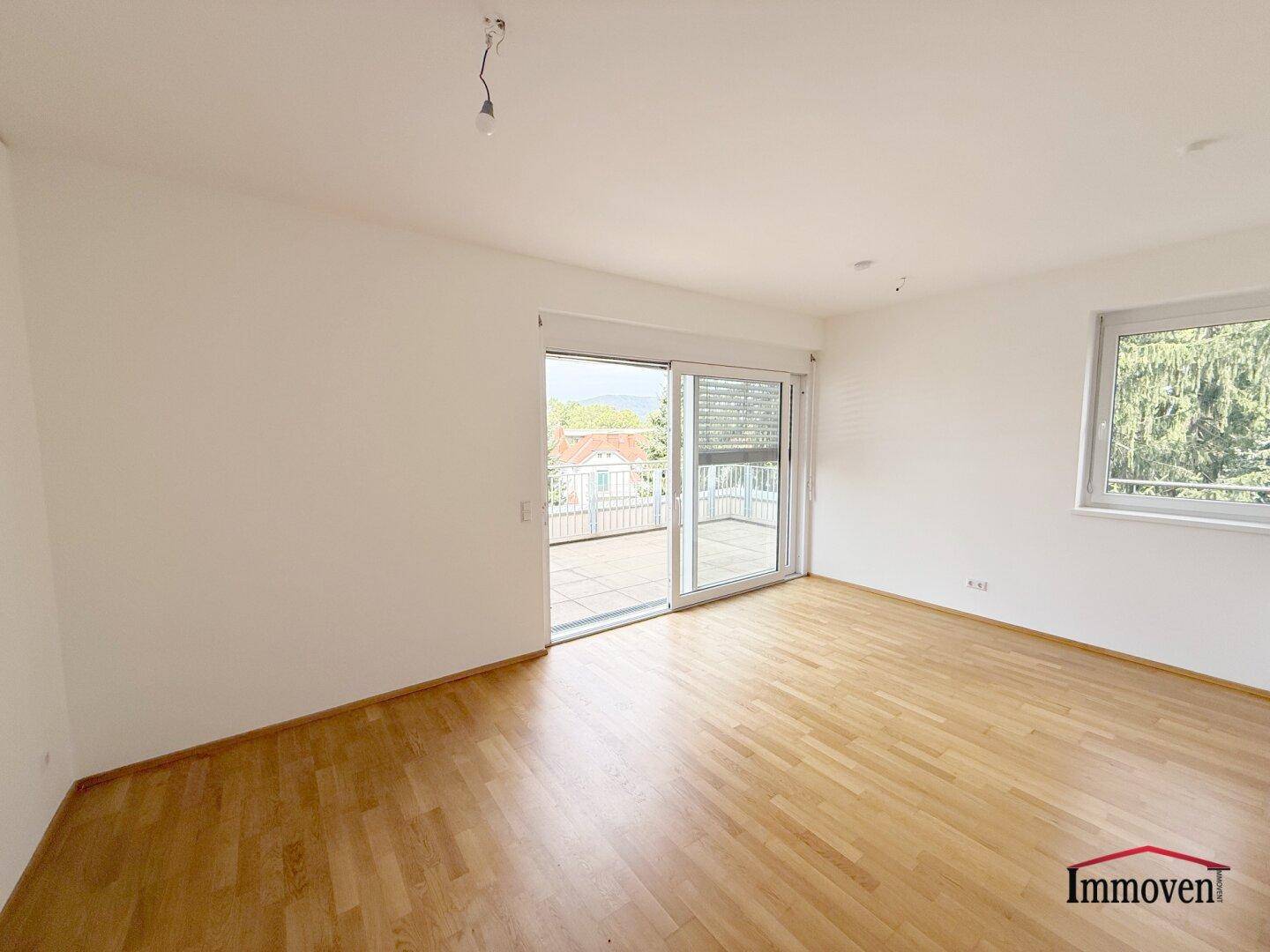 Geräumiger, heller Raum mit Holzboden und großen Schiebetüren, die zur Terrasse führen.