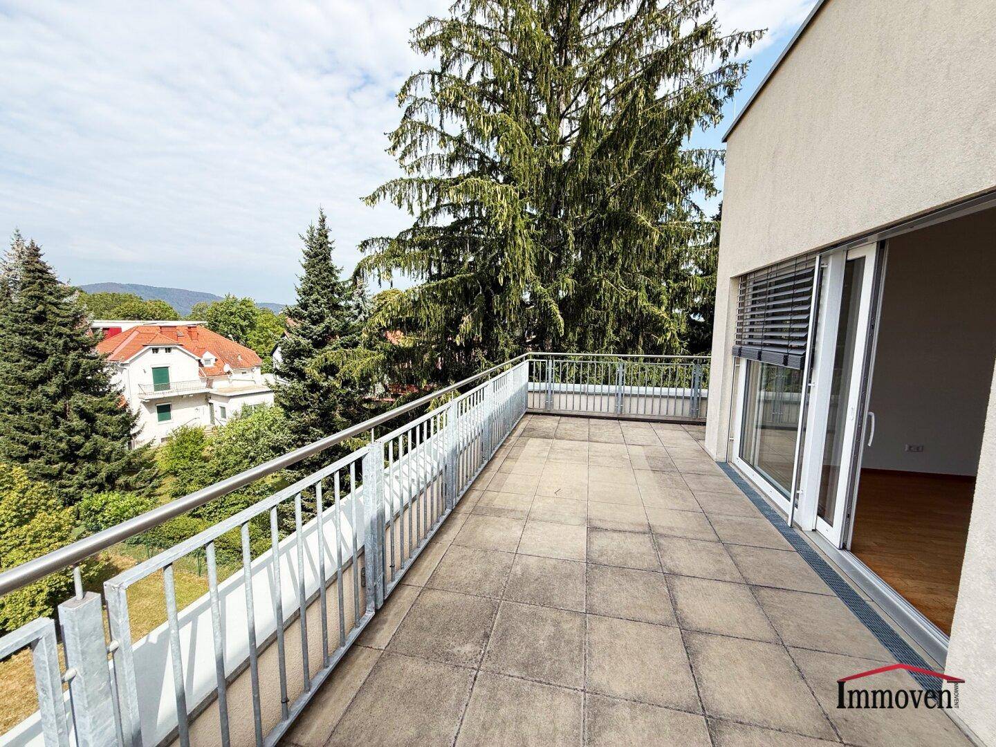 Weitläufige Dachterrasse mit Fliesenboden und weitem Blick über Bäume und die Umgebung.
