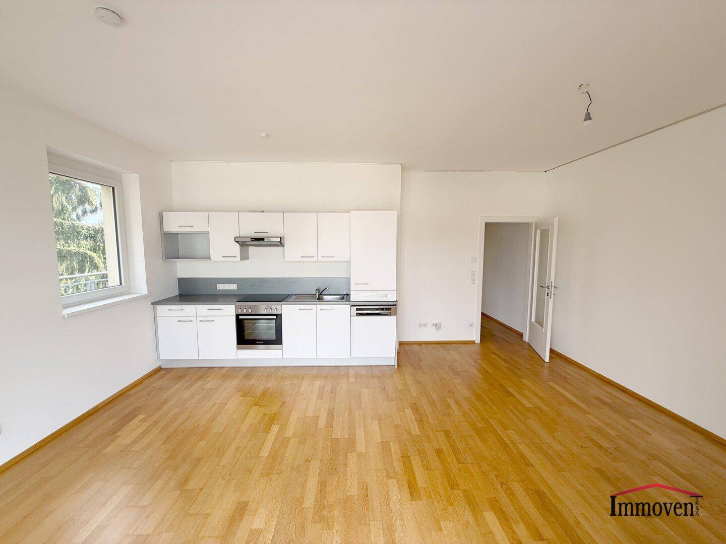 Helle Küche mit weißer Einbauzeile, Holzboden und offenem Zugang zu weiteren Räumen.