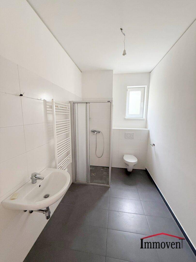 Modernes Badezimmer mit dunklen Fliesen, Dusche, WC, Waschbecken und beheiztem Handtuchhalter.
