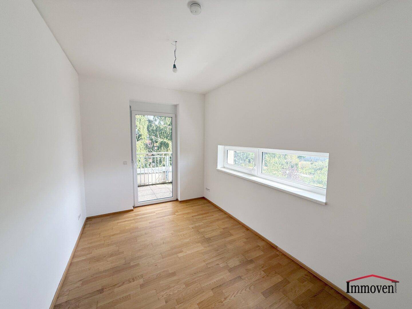Helles Schlafzimmer mit Holzboden, Fenster und Zugang zu einem kleinen Balkon.