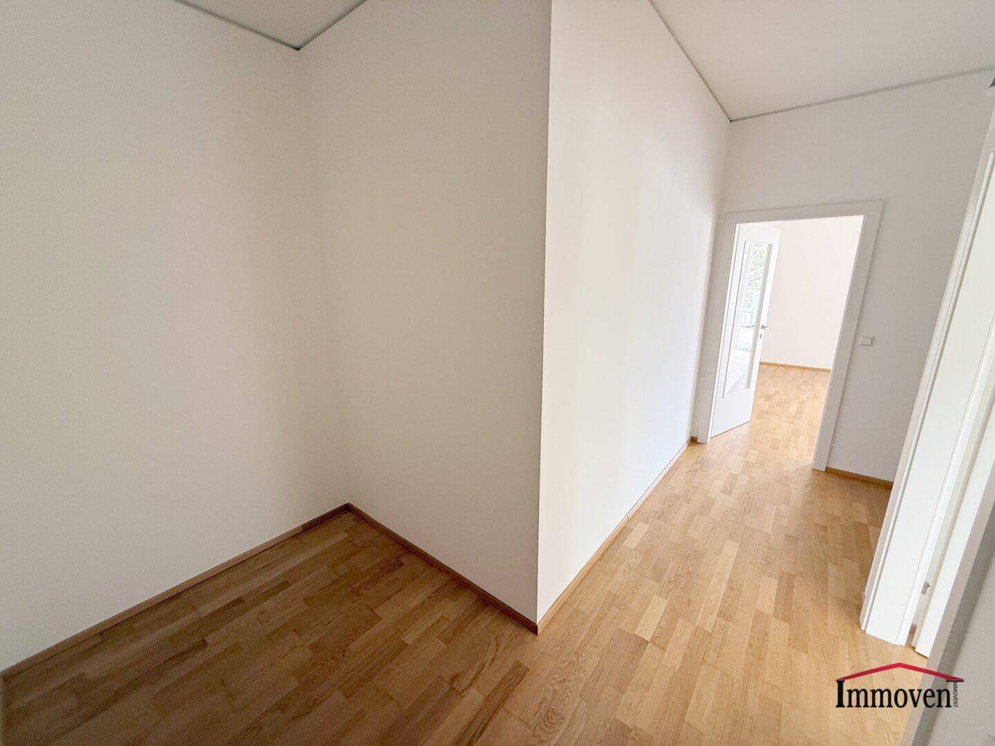 Heller Flur mit Holzboden und weiß gestrichenen Wänden, der zu weiteren Räumen führt.
