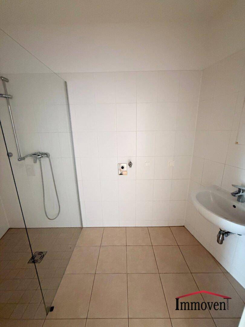 Modernes Badezimmer mit weißen Fliesen, einer begehbaren Dusche und einem Waschbecken.