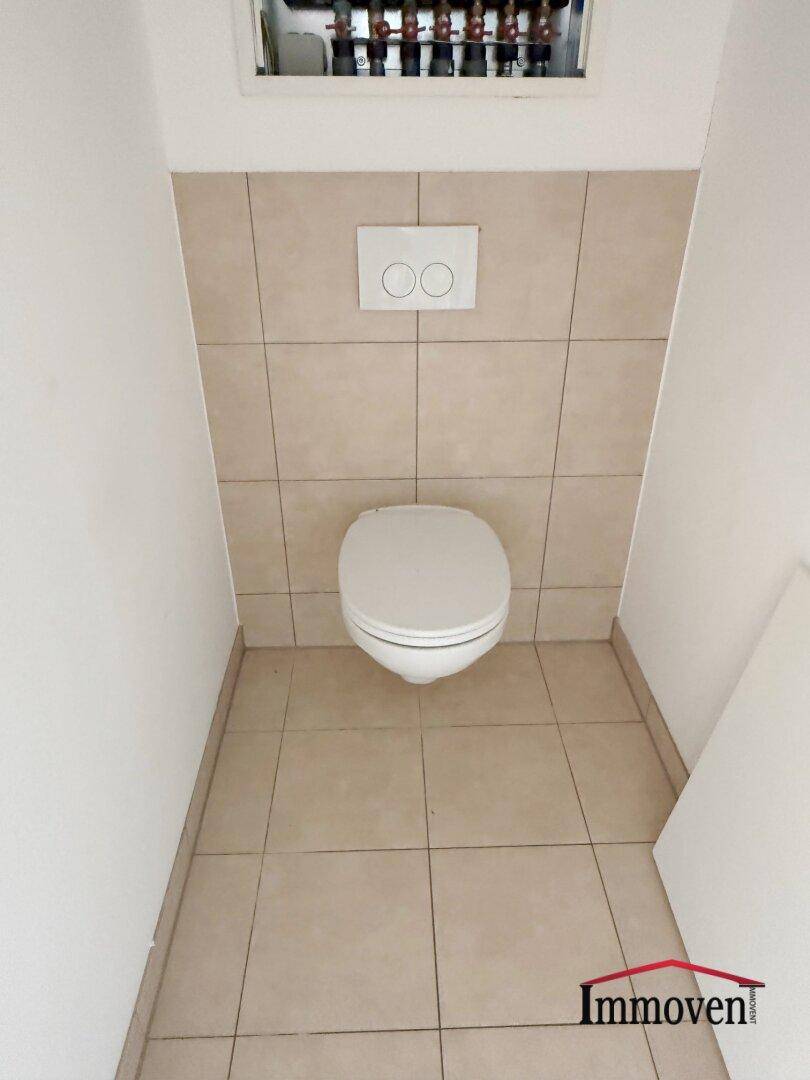 Separates WC mit wandhängender Toilette und beigefarbenen Fliesen, sauber und funktional.