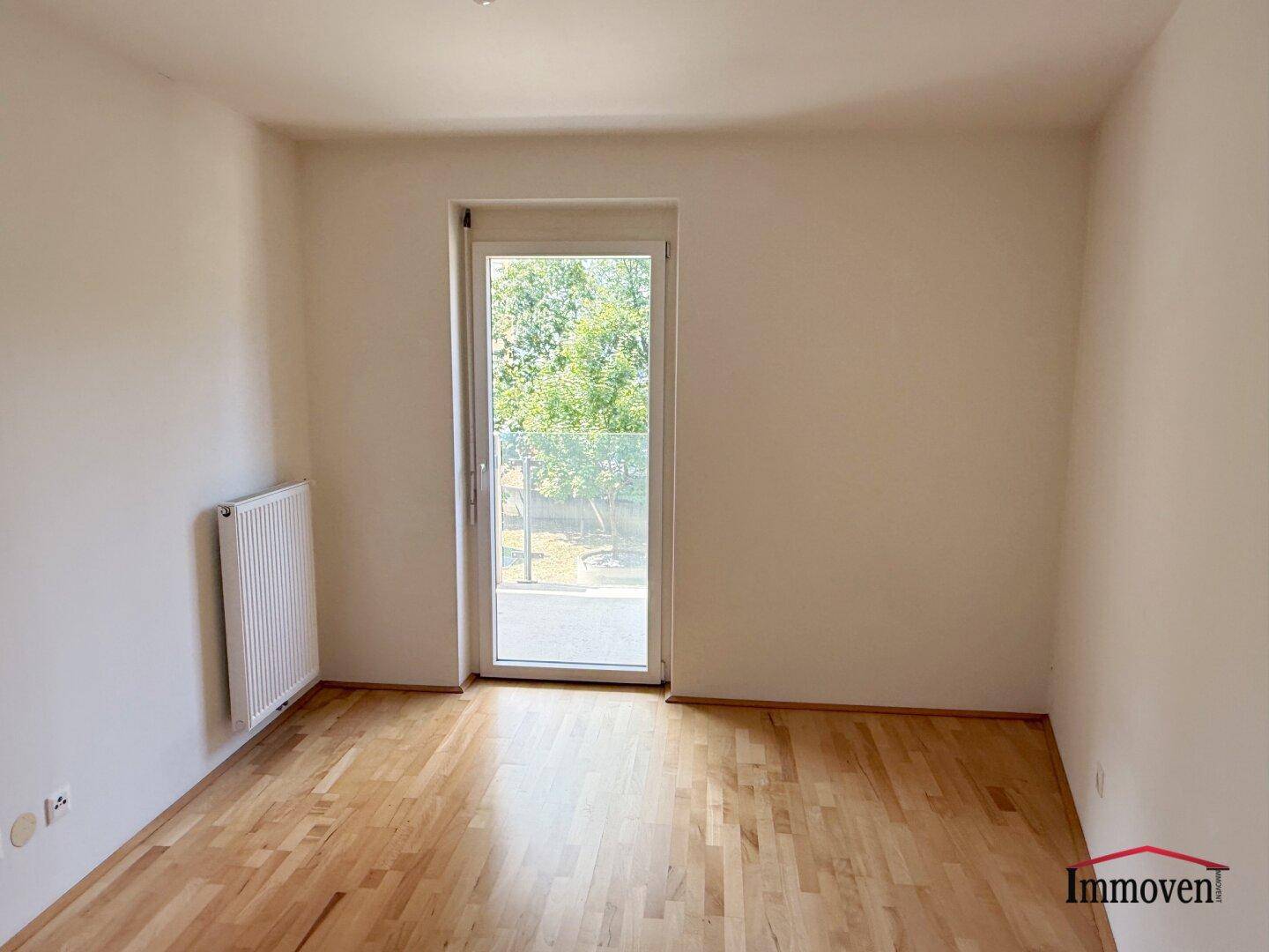 Helles Zimmer mit Parkettboden und Zugang zu einem Außenbereich, ideal als Schlaf- oder Arbeitszimmer.