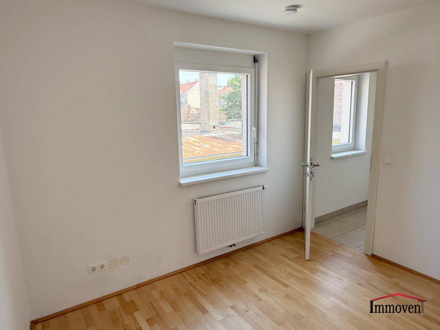Freundliches Zimmer mit Parkettboden und Fenster, das viel Tageslicht hereinlässt.