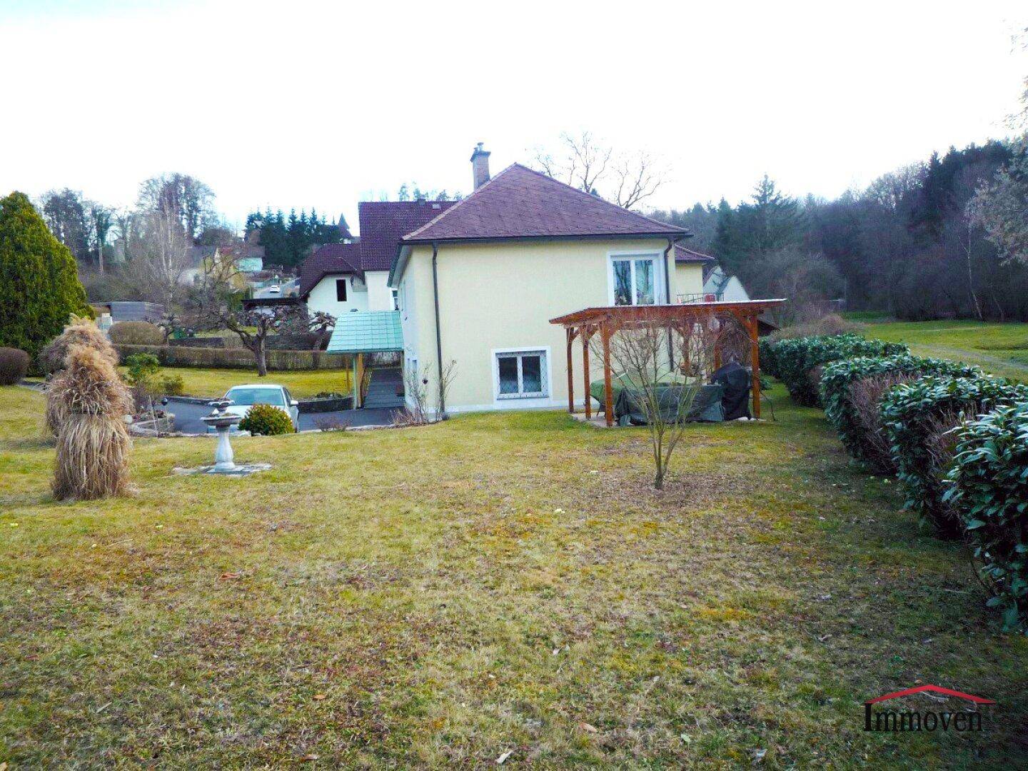 Rückansicht des Hauses mit weitläufigem Garten, gepflegten Hecken und einer Holzpergola.