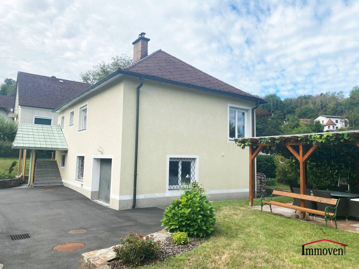 Seitenansicht des Hauses mit Gartenbereich, Pergola und Sitzgelegenheiten im Grünen.