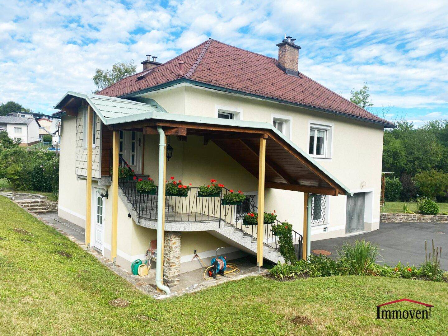 Ansicht des Hauses mit Außentreppe, überdachtem Eingangsbereich und Blumenkästen.