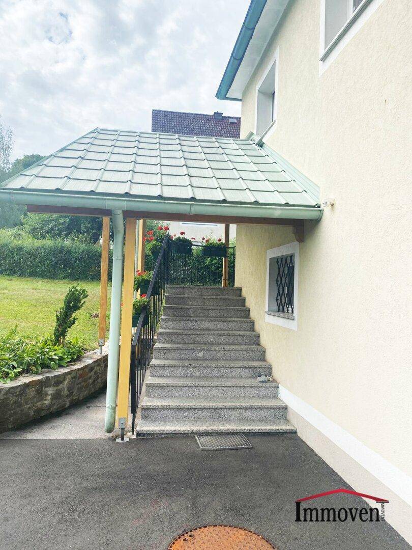 Überdachte Außentreppe mit Geländer, die zum oberen Stockwerk des Hauses führt.
