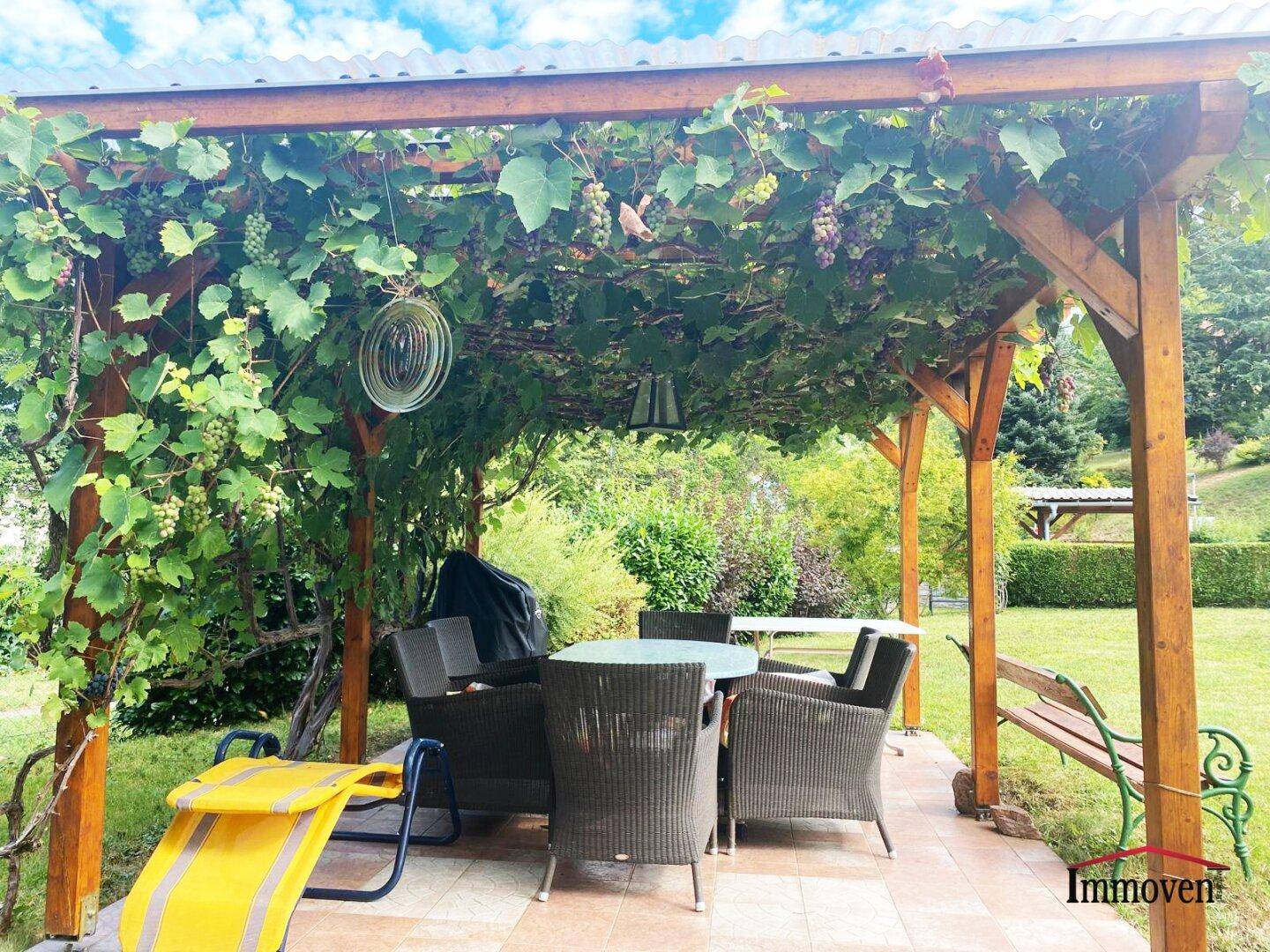 Detailansicht der begrünten Pergola mit Esstisch und Stühlen im Gartenbereich.