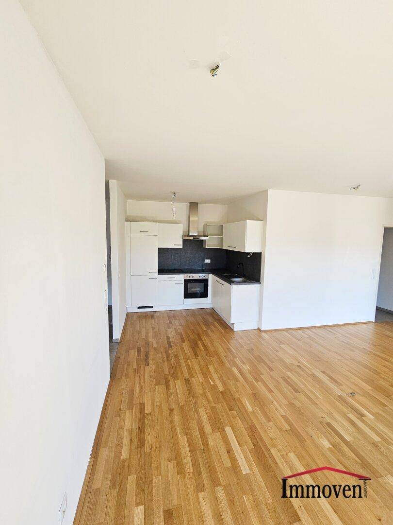 Moderne Einbauküche mit weißen Schränken und dunkler Arbeitsplatte, offen zum Wohnbereich gestaltet.