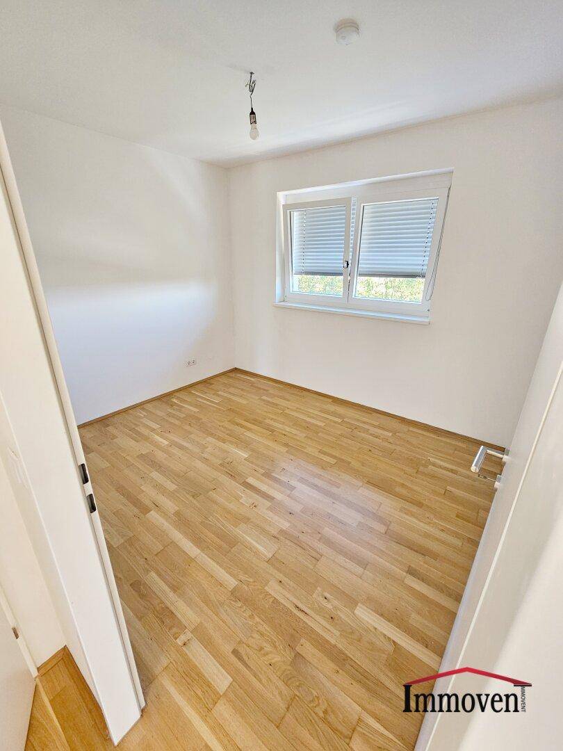 Helles Schlafzimmer mit Holzparkett und einem Fenster, das viel Tageslicht in den Raum lässt.