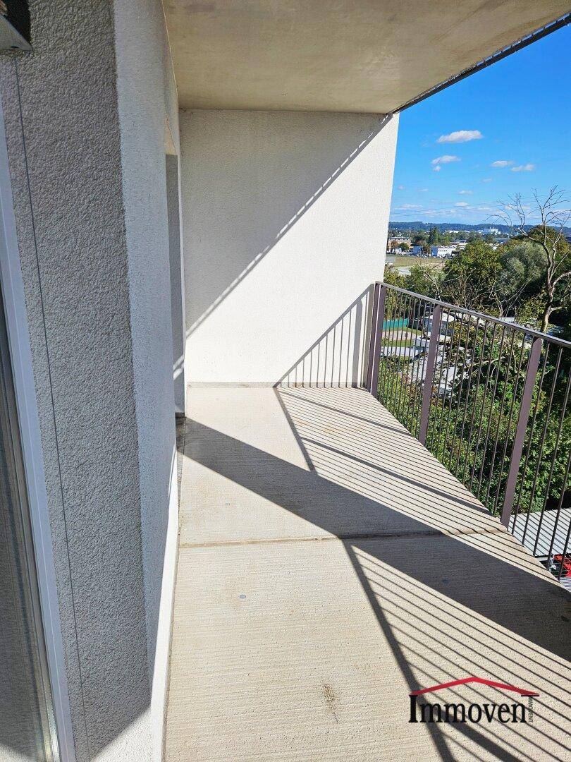 Sonniger Balkon mit Betonboden und Metallgeländer, bietet einen weiten Blick auf die Umgebung.