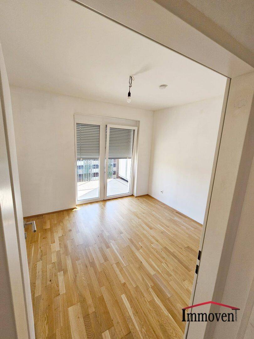 Weiteres helles Schlafzimmer mit Parkettboden und großem Fenster, das den Raum mit Licht füllt.