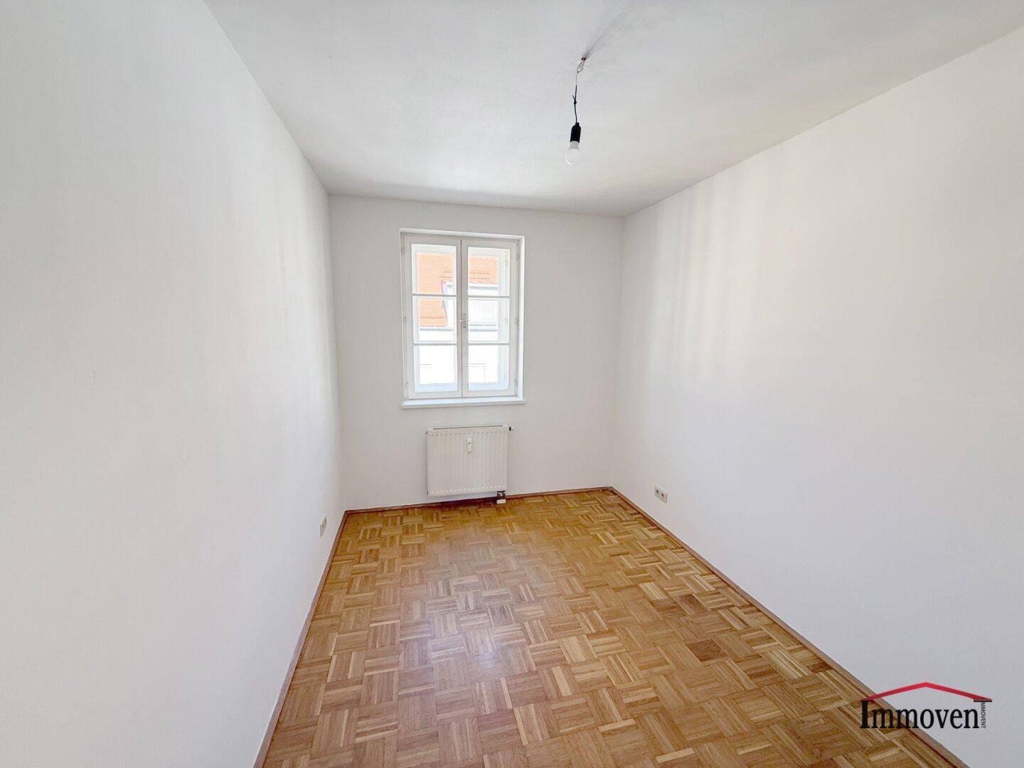 Helles Zimmer mit Parkettboden und einem Fenster, ideal als Schlaf- oder Arbeitszimmer.
