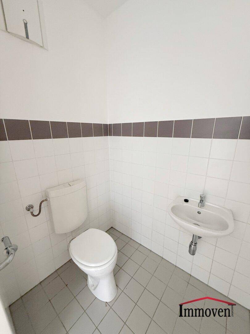 Separate Gästetoilette mit WC, kleinem Waschbecken und weißen Fliesen.