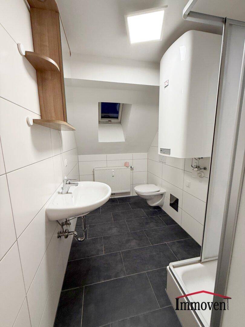 Modernes Badezimmer mit dunklen Fliesen, weißer Keramik und einer Dusche unter einer Dachschräge.