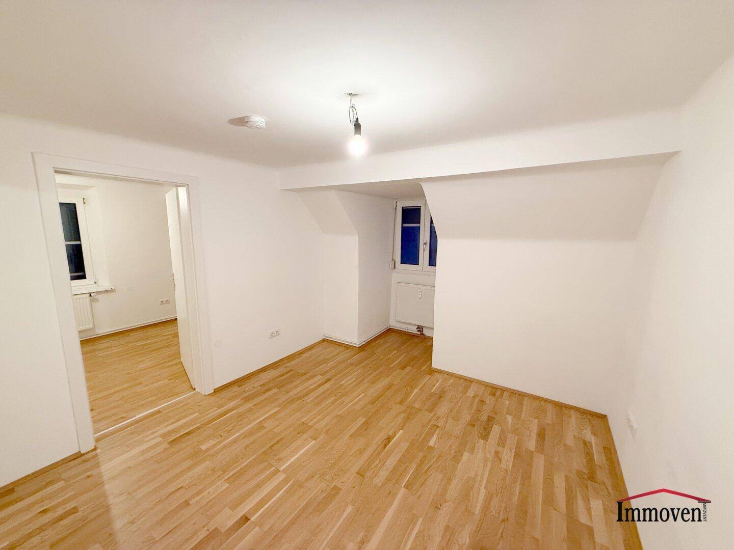 Geräumiges, helles Zimmer mit Parkettboden und Zugang zu einem weiteren Raum.