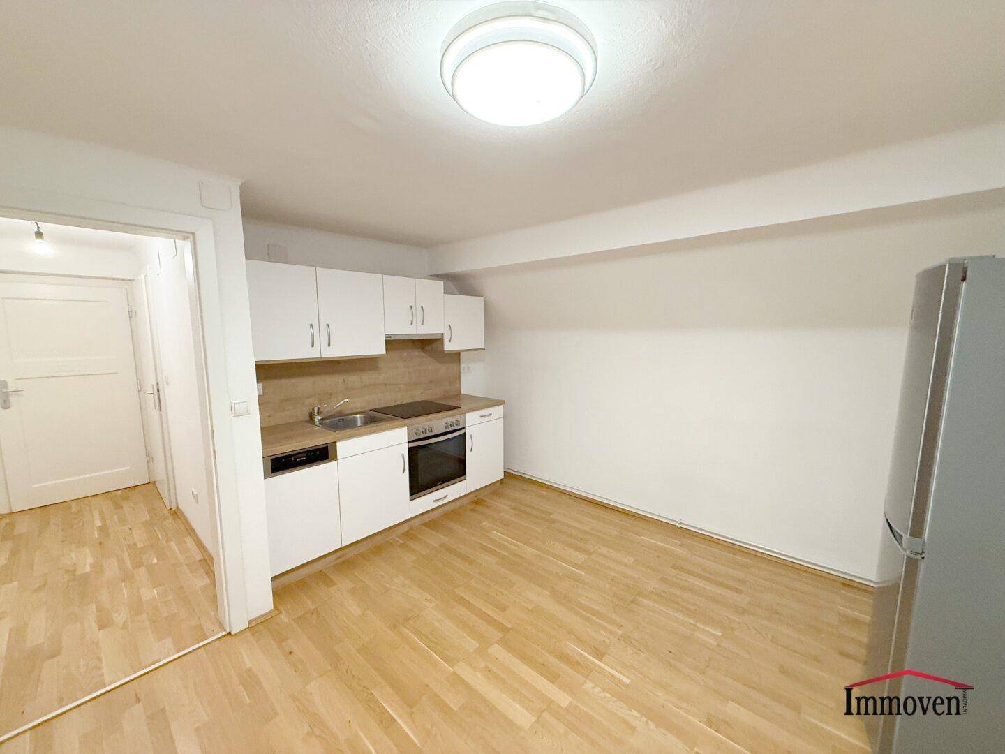 Funktionale Küchenzeile mit weißen Schränken, Spüle, Herd und Kühlschrank in einem hellen Raum.