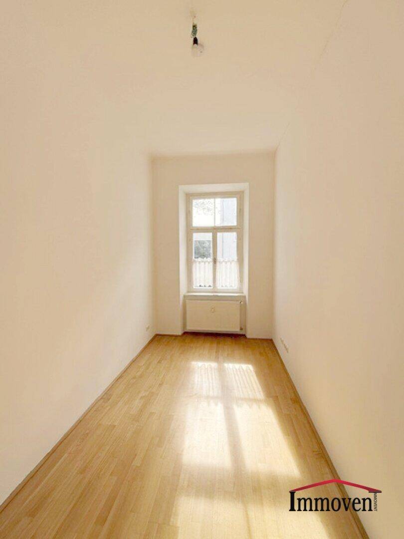 Langes, schmales Zimmer mit Parkettboden und einem Fenster am Ende, das den Raum erhellt.