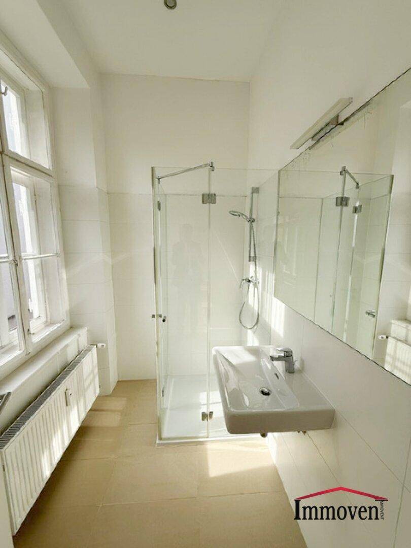Helles Badezimmer mit moderner Glasdusche, Waschbecken und großen Fenstern für viel Tageslicht.