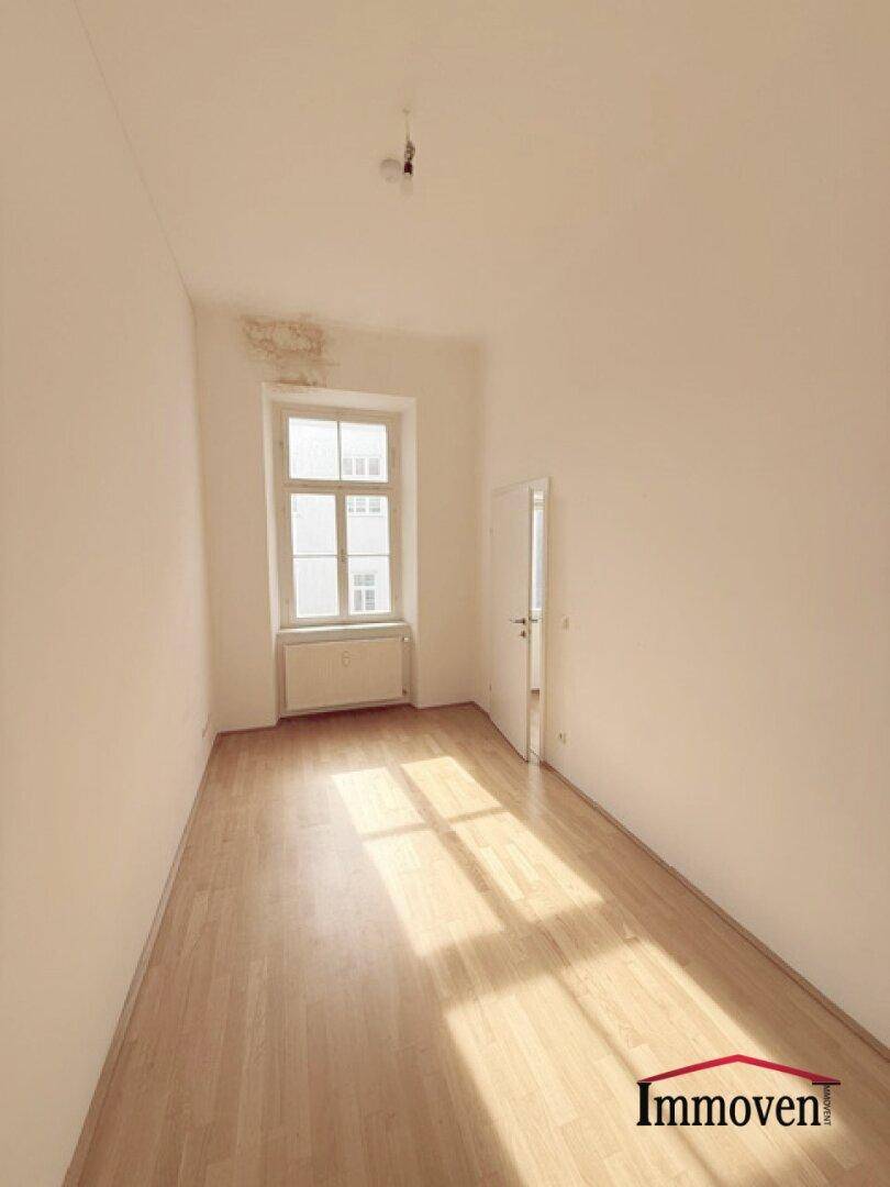 Sonniger, leerer Raum mit Parkettboden und einem Fenster, das Lichtmuster auf den Boden wirft.