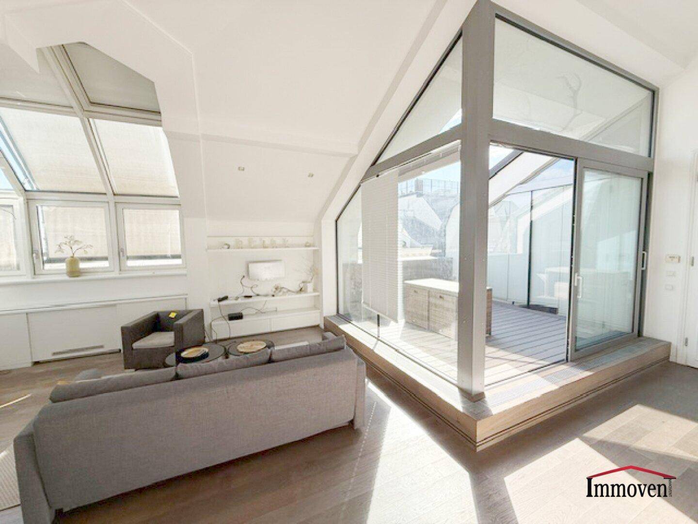 Geräumiges Wohnzimmer mit bequemer Couch und großen Fenstern zur Dachterrasse.
