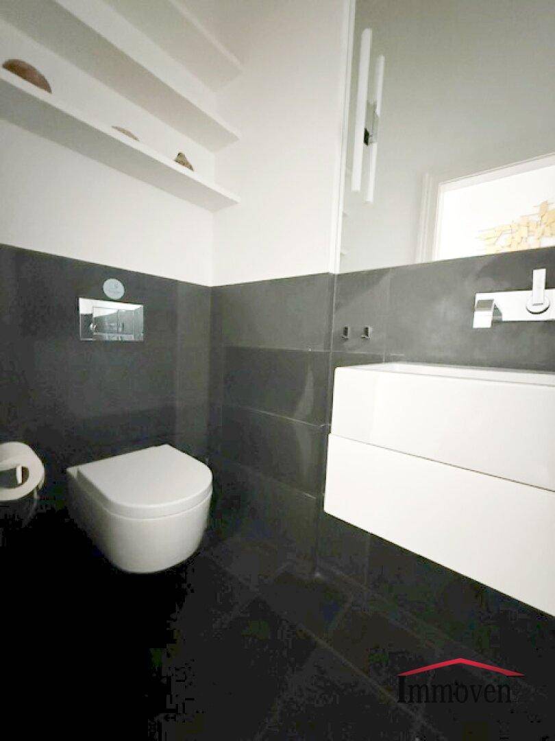 Separates WC mit modernen dunklen Fliesen und wandmontierter Toilette.