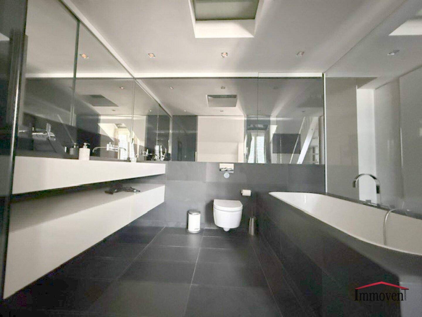 Luxuriöses Badezimmer mit Doppelwaschbecken, Badewanne und dunklen Fliesen.