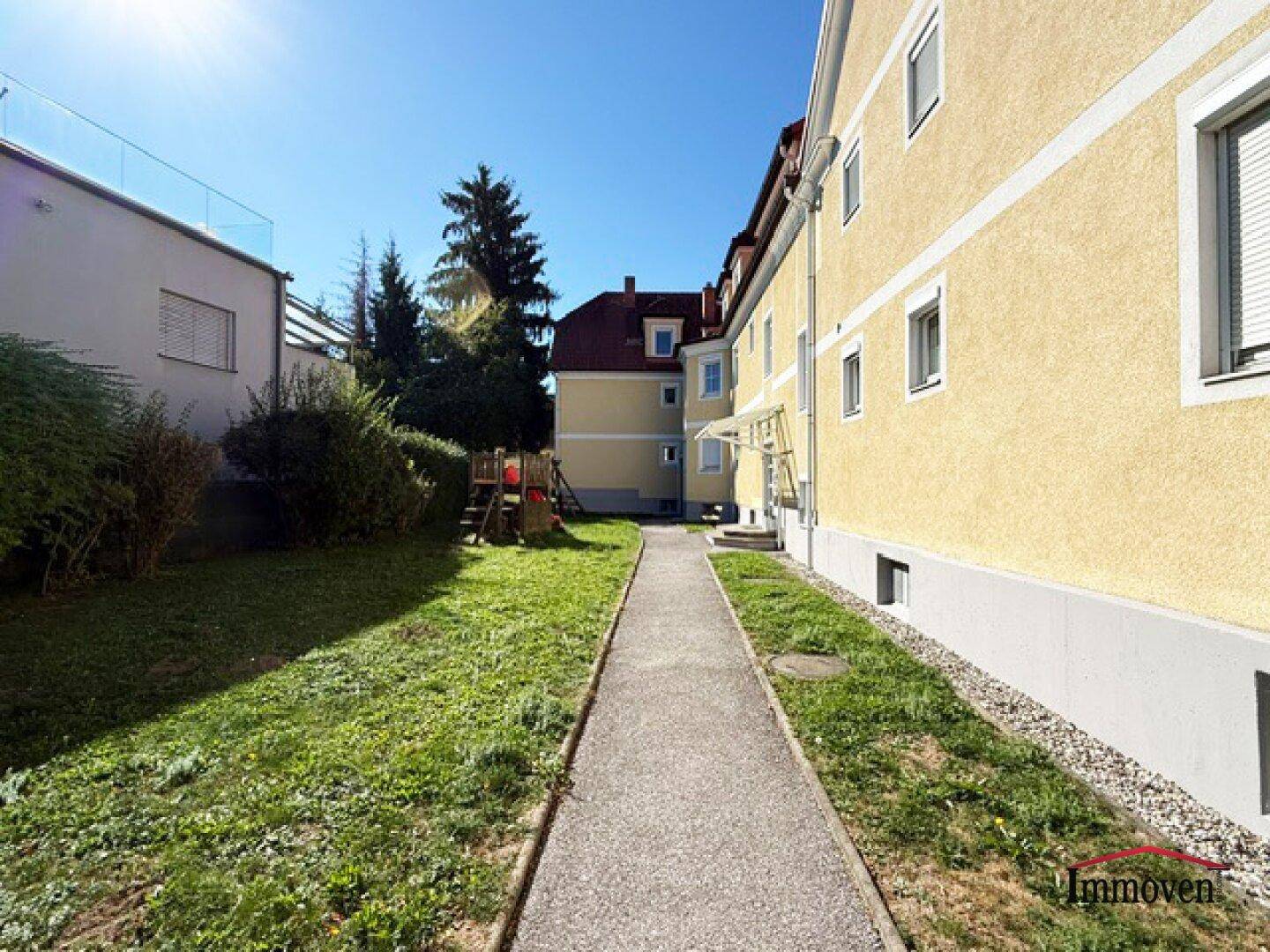 Gemeinschaftsgarten mit Spielplatz und gepflegter Rasenfläche hinter dem Gebäude.